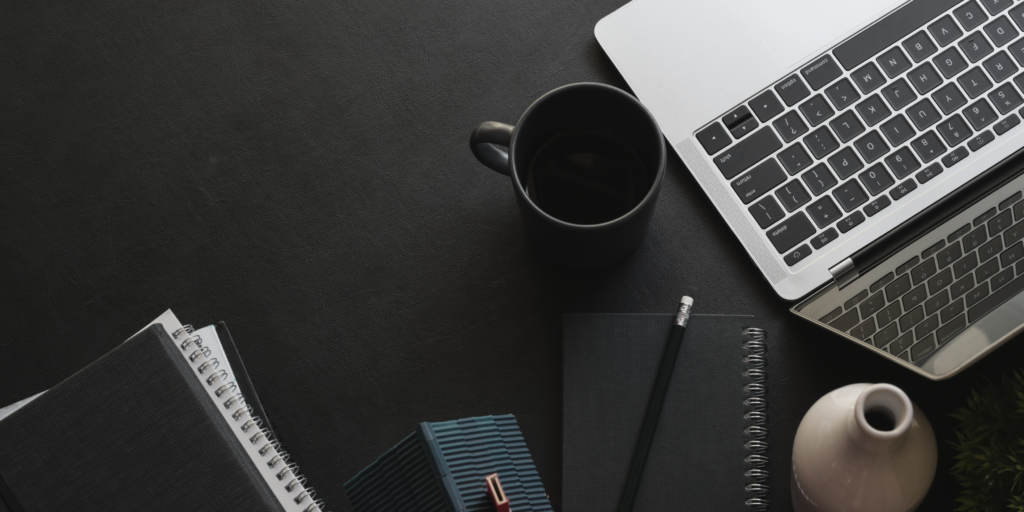 Top view of a powered-on laptop, black coffee mug, and notebooks on a dark desk — ideal workspace for laptop or tablet troubleshooting.